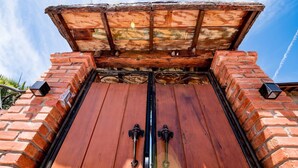 Une grande porte à deux battants en bois, dotée de poignées en métal, encadrée par un mur de briques et surmontée d’un toit en bois.