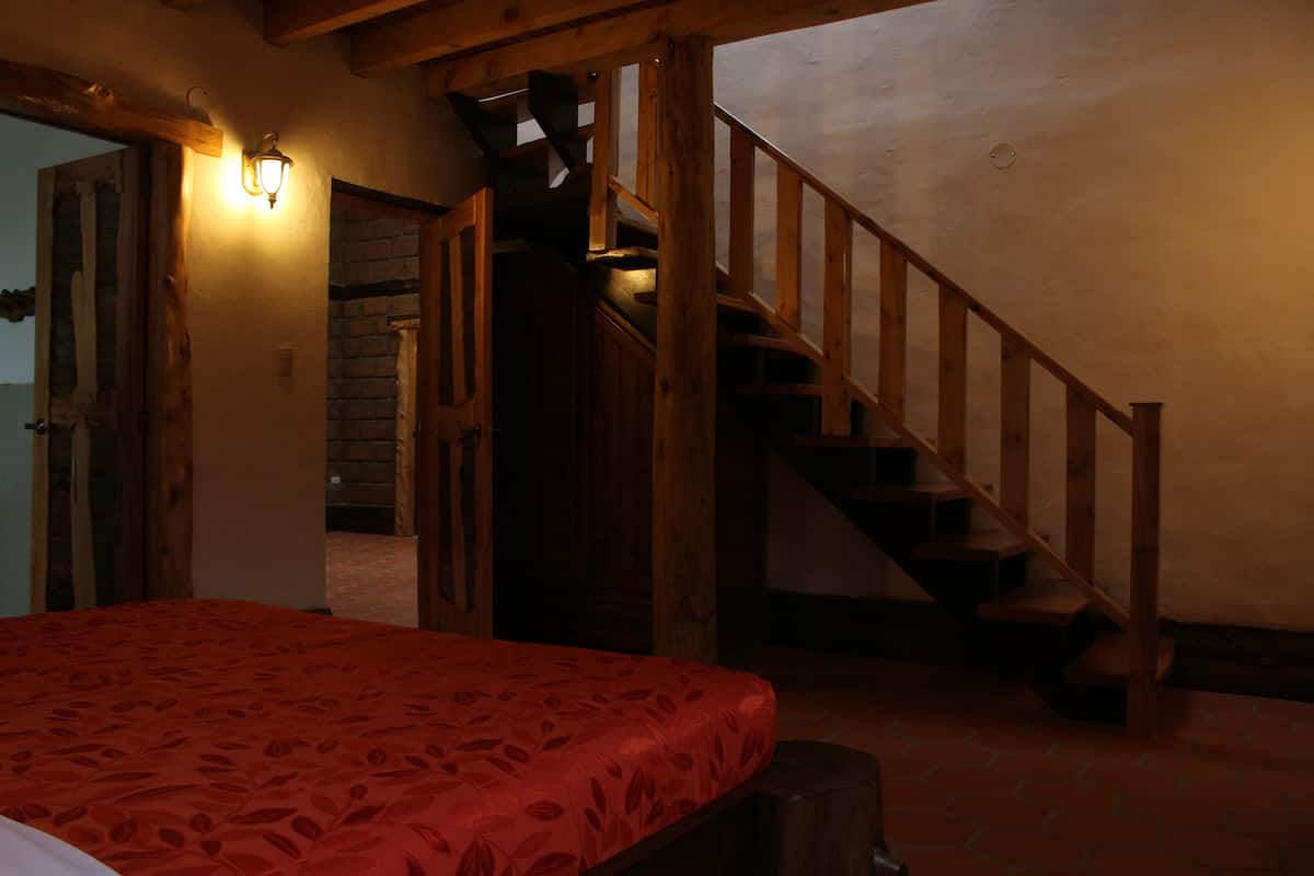 A bedroom with a wooden staircase, a red bedspread, and a brick wall.