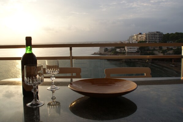A table with a bottle, glasses, and a bowl on a balcony overlooking a cityscape and body of water. - APARTMENT ON THE SEA IN SALOU (Salou)