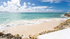 Una playa con aguas turquesas cristalinas, una orilla arenosa y afloramientos rocosos.