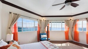 Un dormitorio espacioso con una cama grande, un sillón azul y vistas al océano a través de amplios ventanales.