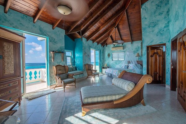 A spacious room with a large bed, wooden furniture, and a view of the ocean. - Ambrosia Villa (Shoal Bay)