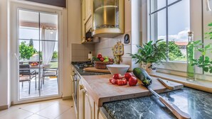 A modern kitchen with a large window, a dining area with outdoor seating, and a variety of fresh produce on the counter. - Gorgeous home in Marcana (Marcana)