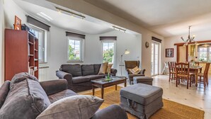 A spacious living room with a large sofa, a coffee table, and a dining area with wooden chairs and a table. - Gorgeous home in Marcana (Marcana)
