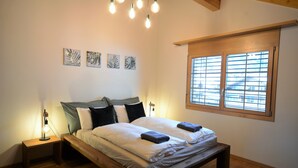 Un dormitorio con cama de madera, mesitas de noche, lámpara colgante y ventana con persianas.