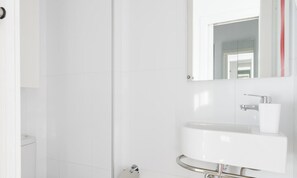 A bathroom with white tiles, a sink, a mirror, and a toilet.