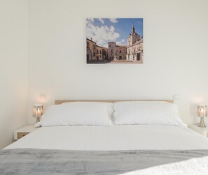 Une chambre à coucher avec un lit, deux tables de chevet et un tableau représentant une scène de rue accroché au mur.