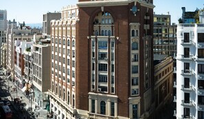 Un edificio histórico con una torre prominente en esquina, múltiples ventanas y un letrero que indica un hotel llamado "Charming Gran Vía - Callao".