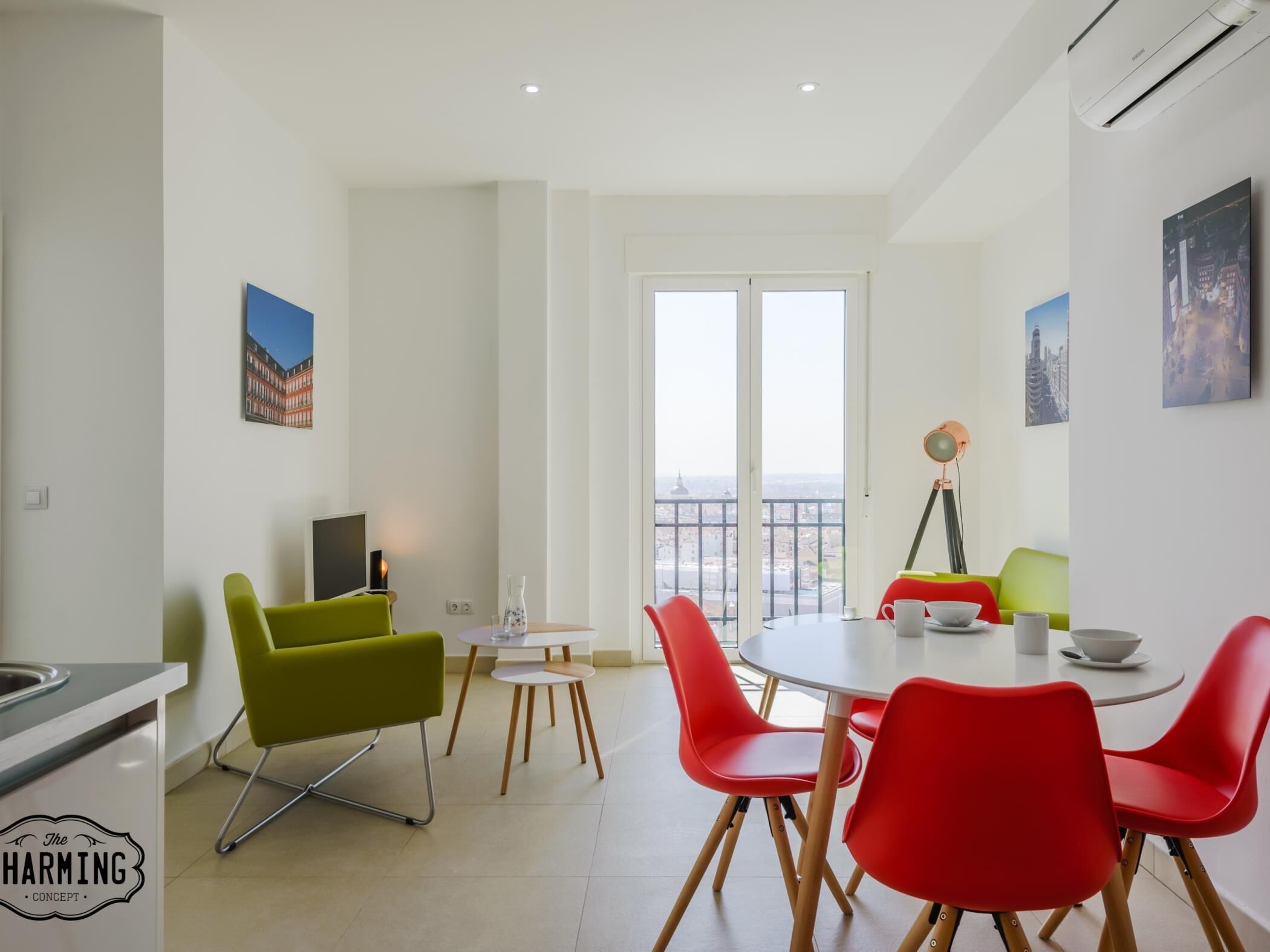 Un salon moderne avec un coin repas, comprenant une grande fenêtre offrant une vue sur la ville, un téléviseur et un lampadaire sur trépied.