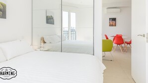 Et moderne hotelværelse med en stor seng, en skydedør til en balkon og et spiseområde med røde stole.