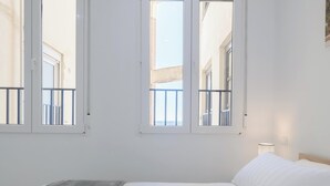 Une chambre à coucher avec un lit, deux fenêtres et une vue sur des immeubles.