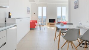 Une cuisine moderne avec des meubles blancs, un coin repas comprenant une table et des chaises, et un balcon offrant une vue sur la ville.