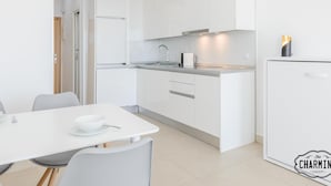 Une cuisine moderne avec des meubles blancs, un évier en acier inoxydable et une table à manger blanche assortie de chaises.