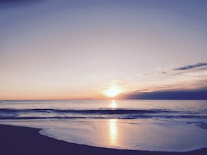 A beach at sunset with the sun low on the horizon, calm sea, and a clear sky. - Steps to a private beach. Ocean and bay views from decks. (Bethany Beach)