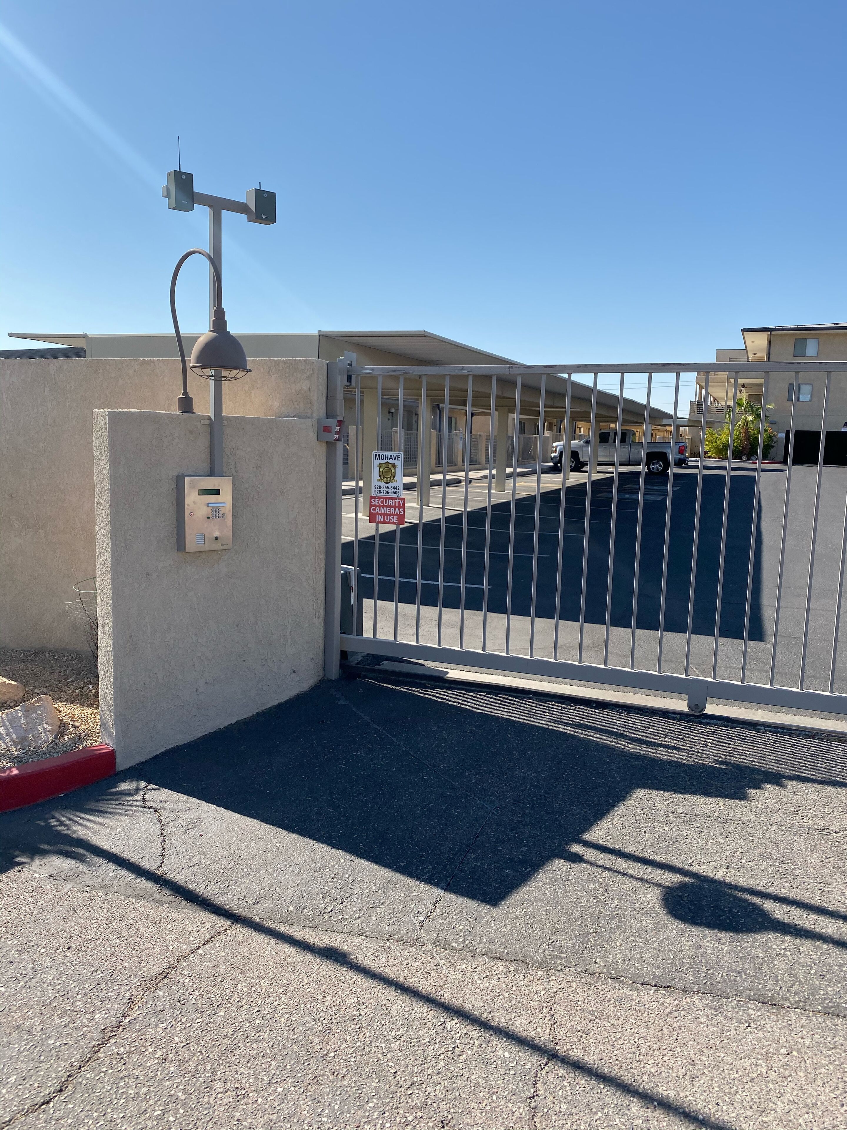 Una entrada con puerta cerrada, cámaras de seguridad, una cerca metálica y un edificio al fondo.