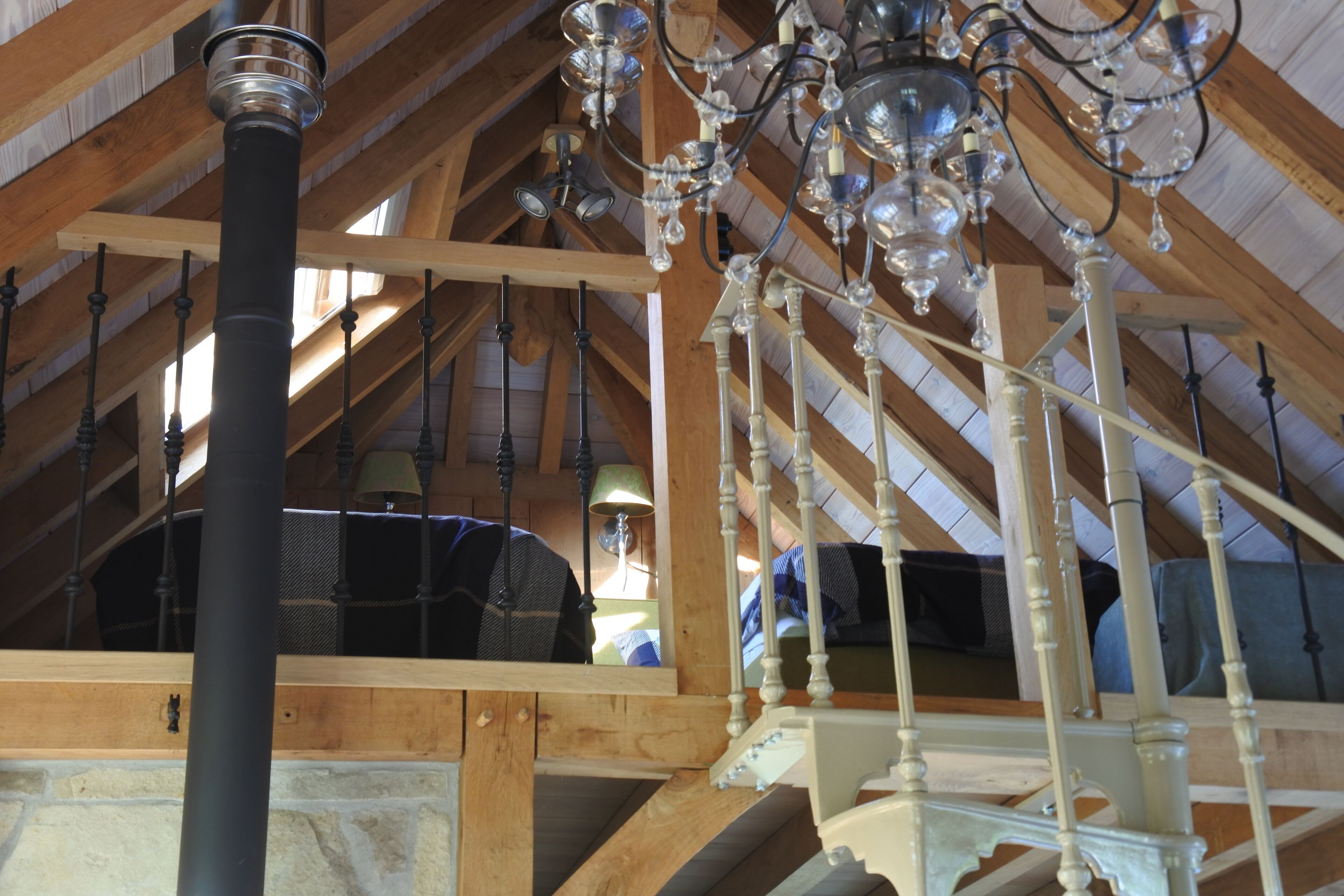 An attic room with exposed wooden beams, a black pipe, and a white staircase.