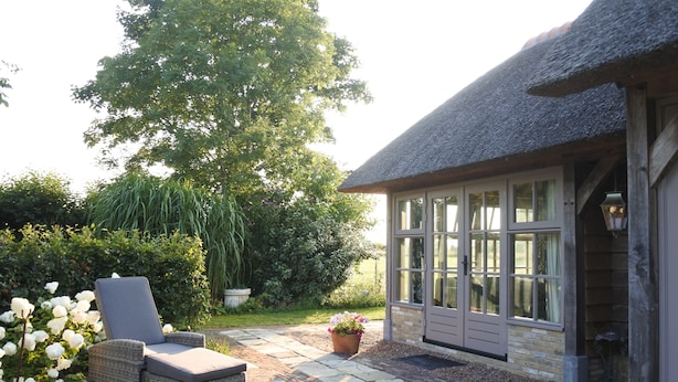 Een terras met een rieten stoel, een potplant en een gebouw met grote ramen en een rieten dak.
