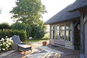 A patio with a wicker chair, a potted plant, and a building with large windows and a thatched roof. - A vacation home in a quiet rural setting (Westerland)