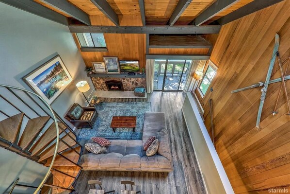 A spacious loft with a stone fireplace, a large gray sofa, and a spiral staircase.