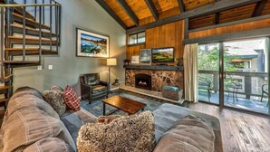 A spacious living room with a fireplace, a staircase, and a balcony with outdoor furniture. - Lakeland 40 Beachfront 1BR + Loft 1BA (South Lake Tahoe)