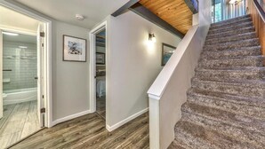 Un escalier avec des marches en bois et une rampe blanche, menant à une pièce dotée d’une porte blanche et d’un tableau encadré au mur.
