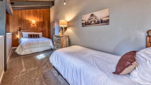 Une chambre avec deux lits, une tête de lit en bois, une table de chevet avec une lampe et un tableau accroché au mur.