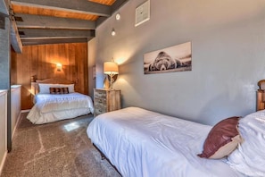 Ein Schlafzimmer mit zwei Betten, einem hölzernen Kopfteil, einem Nachttisch mit Lampe und einem Wandbild.