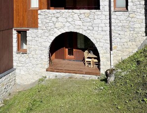 A stone building with a wooden deck and a table with chairs. - Le Portail 27 - Cosy 2-room apartment ski-in ski-out (LES AVANCHERS VALMOREL)