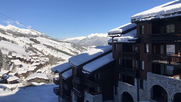 A snow-covered mountain resort with wooden buildings and stone architecture, featuring balconies and a view of the snowy landscape. - Le Portail 27 - Cosy 2-room apartment ski-in ski-out (LES AVANCHERS VALMOREL)