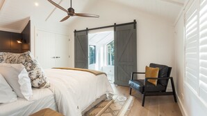 Ein Schlafzimmer mit Bett, Sessel, Deckenventilator und einer großen Schiebetür.