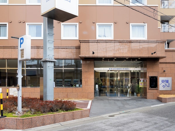 Entrada de hotel con un cartel de estacionamiento, puertas de cristal y un letrero con caracteres japoneses.