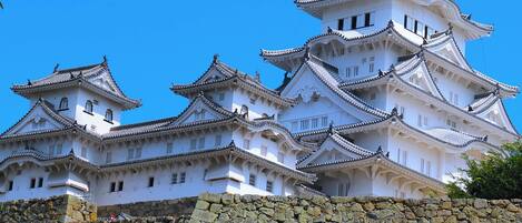 Un château japonais traditionnel, doté de plusieurs niveaux et de murs blancs, entouré d’un mur de pierre.