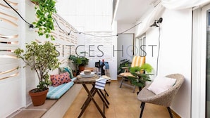 A narrow outdoor space with a table, chairs, potted plants, and a white wall with decorative patterns. - Stylish home with patio 5 mins to beach (Sitges)