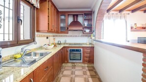 Een kleine keuken met houten kastjes, een roestvrijstalen spoelbak, een inbouwoven en een betegelde spatwand.