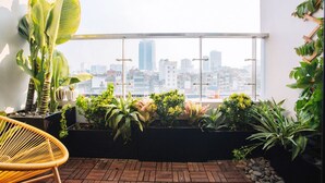 Ein Balkon mit Topfpflanzen, einem Korbstuhl und Blick auf die Stadt.