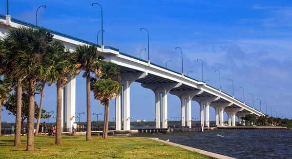 A bridge with white pillars and a blue railing, overlooking a body of water with palm trees and a grassy area. - Adorable single family home 2/1, Sleeps 6, Pet Friendly, Minutes from the Beach (Jensen Beach)