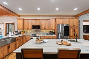 A modern kitchen with wooden cabinets, stainless steel appliances, and a marble island. - Luxury Creekside Cottage, Hot Tub, Fire Pit, 4 Porches, Near Cashiers & Sapphire (Sapphire)