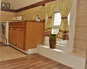 A kitchen with wooden cabinets, a stove, and a window with checkered curtains. - The City Pads: conveniently located, with everything just a short walk away. (Grand Forks)