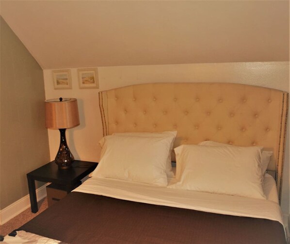 A neatly made bed with white linens and a headboard, a bedside lamp, and two framed pictures on the wall. - The City Pads: conveniently located, with everything just a short walk away. (Grand Forks)