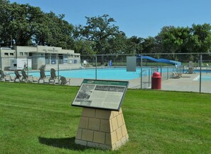 A community park with a swimming pool, a fenced area, and a brick monument with an informational plaque.