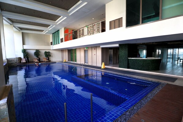 Une piscine intérieure entourée d’une terrasse en bois, un balcon avec une balustrade et un espace d’accueil agrémenté d’un mur végétal.