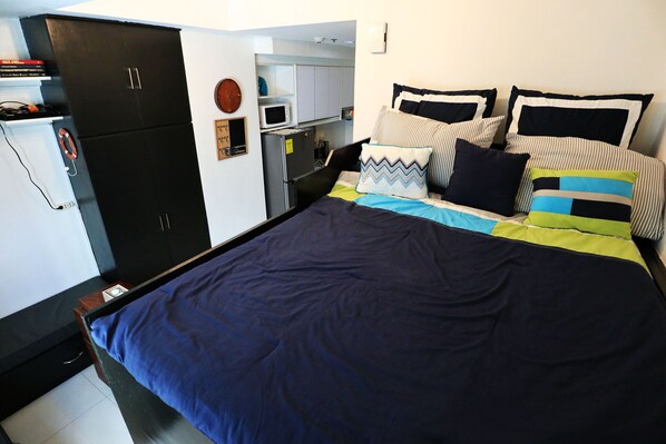 Une chambre à coucher comprenant un lit, des oreillers, une armoire et une petite kitchenette.