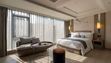 Una habitación de hotel moderna con una cama grande, un sofá, una mesa redonda y un taburete pequeño.