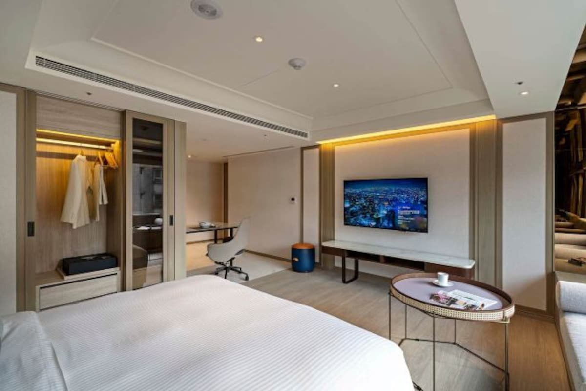 Una habitación de hotel moderna con una cama grande, un escritorio, un televisor y una zona de estar con una pequeña mesa.