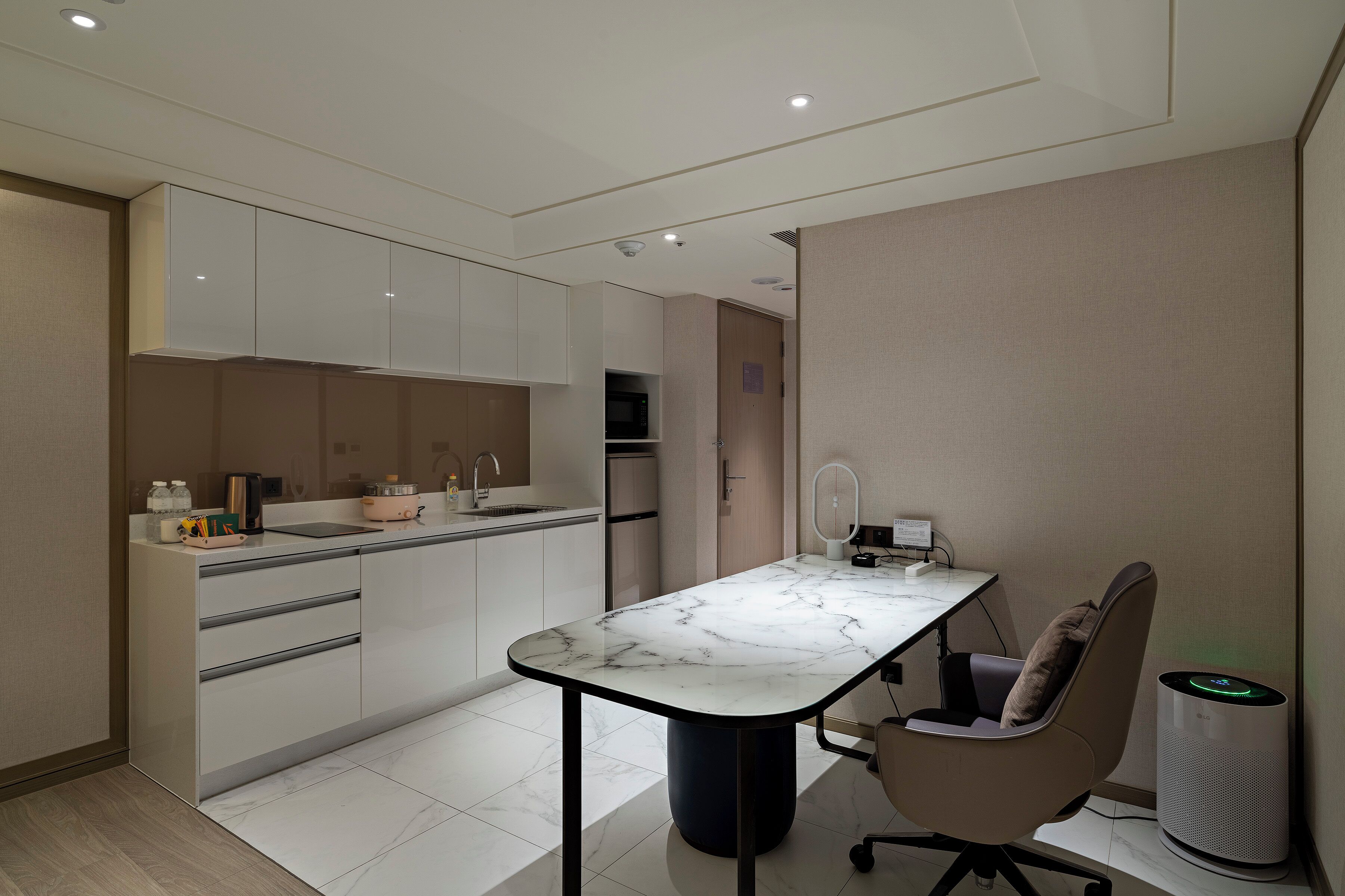 A modern kitchen with a marble countertop, integrated appliances, and a compact dining area with a chair and a smart speaker.