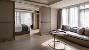 A modern hotel room with a large bed, a sofa, a round table, and a view of the city through sheer curtains. - Hanns House (Taipei)