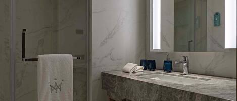 A modern bathroom with a glass shower enclosure, a marble-tiled floor, a large mirror, and a marble countertop with a sink and towel rack.