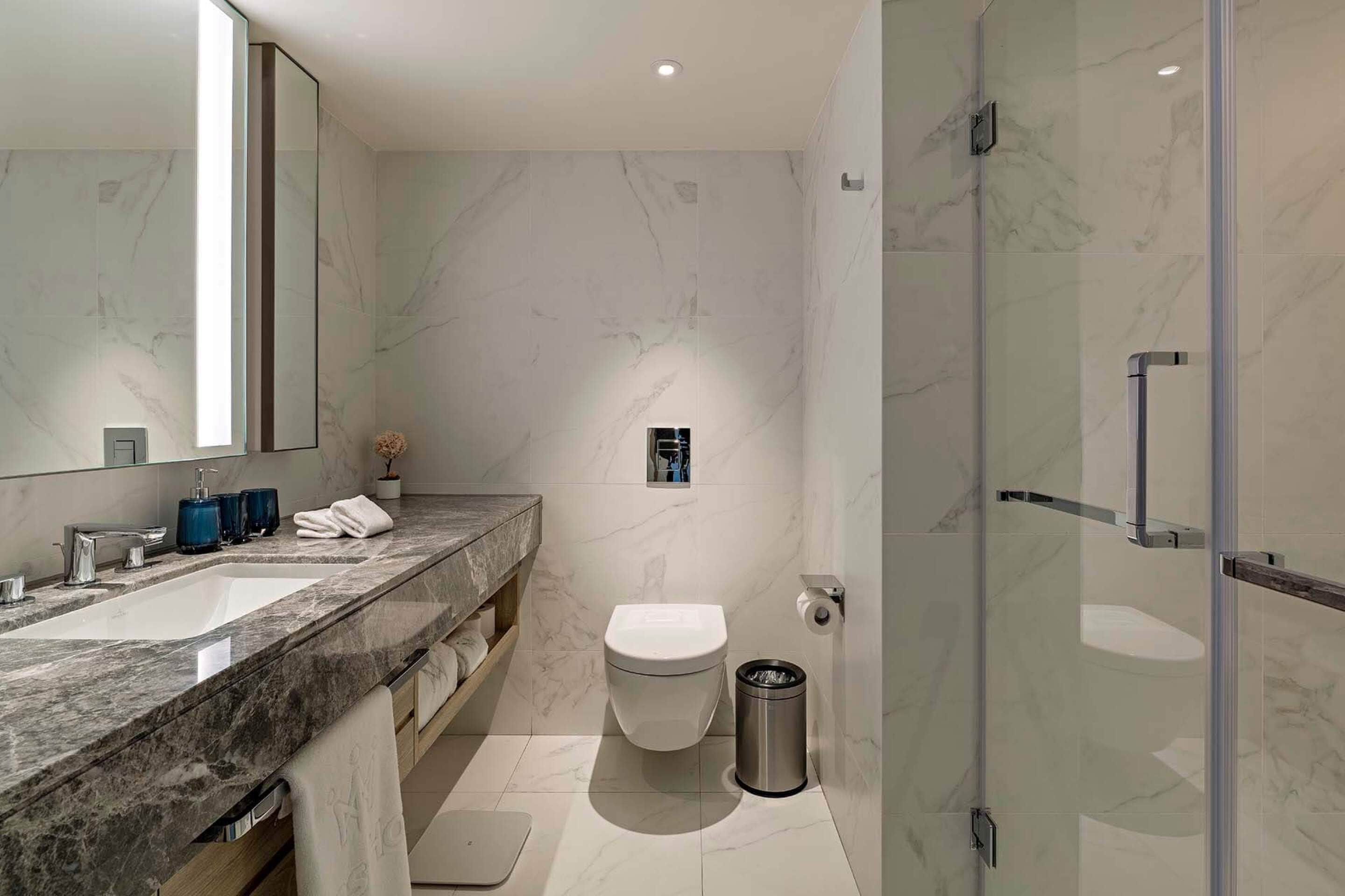 A modern bathroom with a marble countertop, a toilet, and a glass shower enclosure.