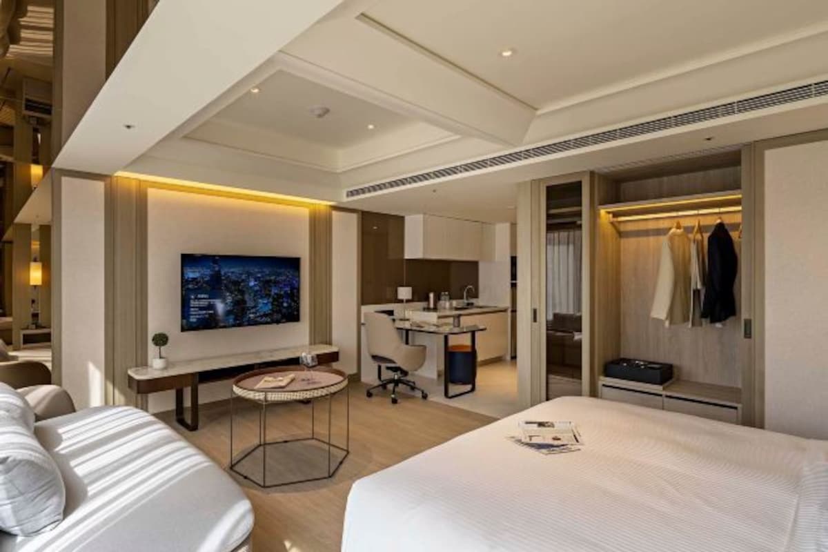 Una habitación de hotel moderna con una cama grande, un escritorio, una televisión y un vestidor.