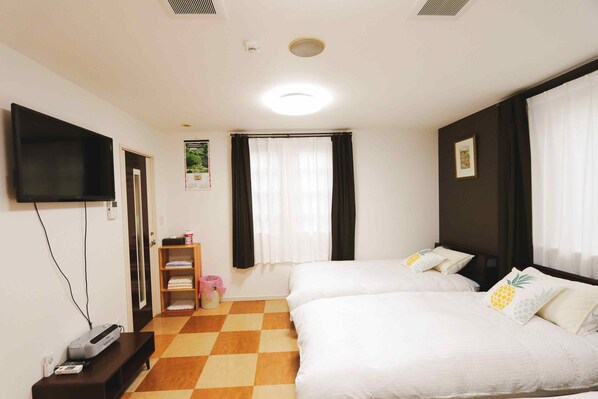 Une chambre d’hôtel avec deux lits, un téléviseur à écran plat, un petit bureau et un sol à carreaux.